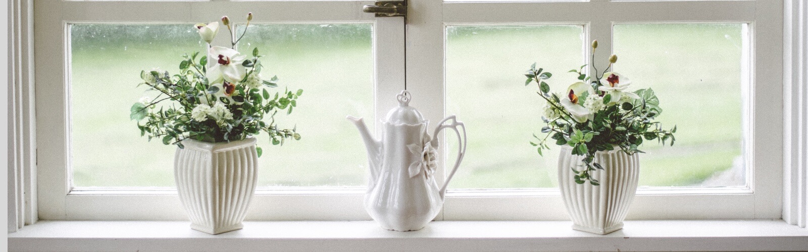 a windowsill holding two flower pots and a white porcelain teapot